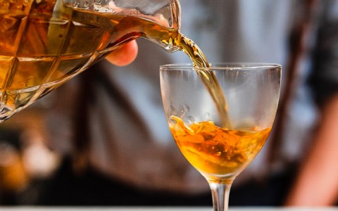bartender pouring an amber spirit into a glass