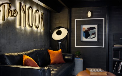 a black couch with orange pillows and a lamp on a black wall