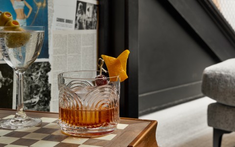 a glass with a drink and a fruit garnish on a checkered surface