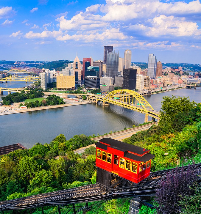 a red trolley on a hill with Duquesne Incline in the background