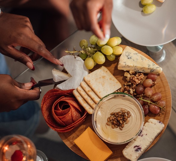 a person cutting a cheese board with grapes and cheese