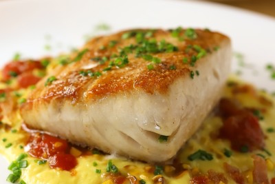 a piece of fish with sauce and green sprinkles